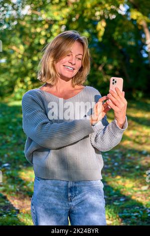 Una donna in un parco in estate parla durante una videochiamata al telefono. Foto di alta qualità Foto Stock