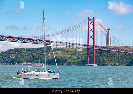 Una foto di una barca a vela nel fiume Tago Tejo, dominata dal Ponte 25 de April e dalla Statua del Cristo Rei Foto Stock