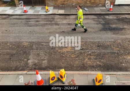 Operaio cammina per la strada con la pala sulla spalla dopo la rimozione meccanizzata della vecchia superficie stradale prima di rifare una strada residenziale a Twickenham, Greater London, UK. (132) Foto Stock
