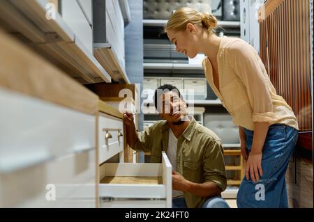 Coppia interracial che sceglie i nuovi mobili della cucina di armadietti nel deposito che guarda i particolari Foto Stock