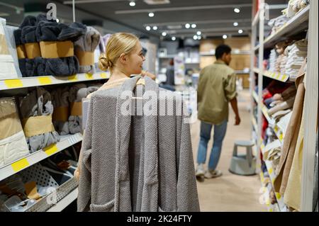 Interracial famiglia coppia cliente scegliere accappatoio in negozio. Donna che acquista vestiti per il marito Foto Stock