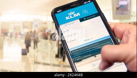 Amsterdam, NED, ottobre 2021: Tenere un telefono con la richiesta di prenotazione dei voli KLM Airlines. Aeroporto offuscato con passeggeri in background. Bo Foto Stock