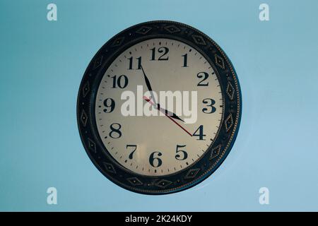 Il vecchio design dell'orologio si trova su una parete blu; la cornice dell'orologio è in legno Foto Stock