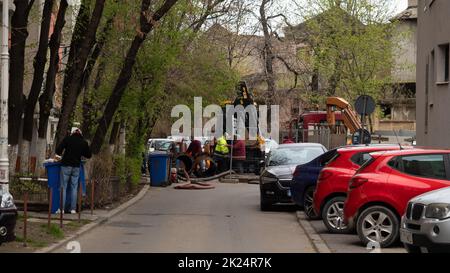 BUCAREST, ROMANIA - 15 maggio 2021: I lavoratori effettuano lavori di riparazione della fogna cittadina. Trattore, riparazione in città, buco nell'asfalto. Foto Stock