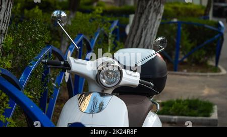 Motocicletta elettrica intelligente bianca a noleggio, parcheggiata sul marciapiede di una città, in attesa che un cliente la noleggi Foto Stock