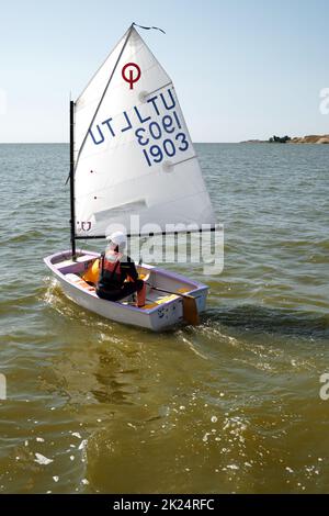 Nida, Lituania - 24 luglio 2021: Bambino giovane che naviga l'Optimist, un piccolo gommone a vela con una sola mano destinato all'uso da parte di bambini e adolescenti Foto Stock