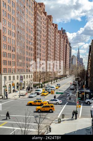 Crocevia a Chelsea, New York City con un sacco di taxi gialli e auto che passano durante la soleggiata giornata invernale, Brown Building facciate nel backgrou Foto Stock