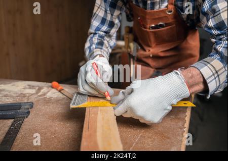 Concetto di lavorazione del legno e del mobile. Il carpentiere in officina contrassegna i dettagli del mobile utilizzando un quadrato, vista ravvicinata. Alto Foto Stock