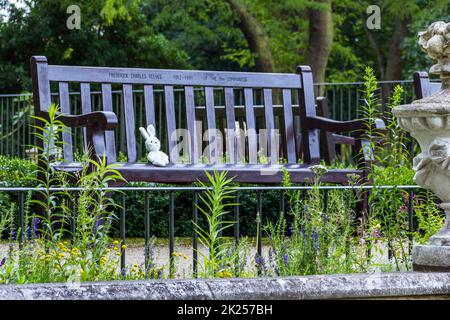 Un coniglio giocattolo perduto siede in preda a una panca di legno in un parco pubblico, Londra, Regno Unito Foto Stock