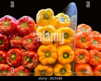 Peperoni freschi misti avvolti in pellicola di cellophane. Peperoni rossi, peperoni gialli, peperoni arancioni. Le cime si chiudono intere. Foto Stock