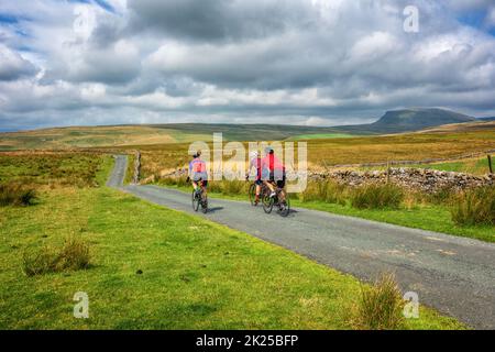 Tre ciclisti maschi che si socializzano in bicicletta su una corsia di campagna sopra Malham Moor con vista sul monte Pen-y-ghent, sullo Yorkshire Dales National Park, North Y Foto Stock