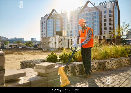 Costruttore che utilizza il caricatore manuale in cantiere Foto Stock