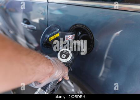 uomo che riempie il serbatoio del carburante della sua auto mentre indossa un guanto di plastica Foto Stock