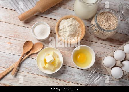 Cornice di ingredienti alimentari per la cottura su fondo bianco. Farina, uova, zucchero e latte in ciotole bianche e di legno . Concetto di cottura e cottura. Foto Stock