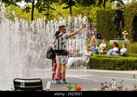 Amsterdam, Paesi Bassi - Agosto 2022: Due persone prendono un selfie mentre si trovano accanto ad una fontana in un giardino pubblico Foto Stock