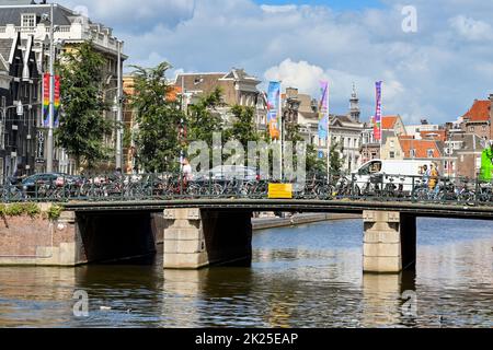 Amsterdam, Paesi Bassi - 2022 agosto: Ponte su uno dei canali della città con biciclette parcheggiate da pendolari Foto Stock