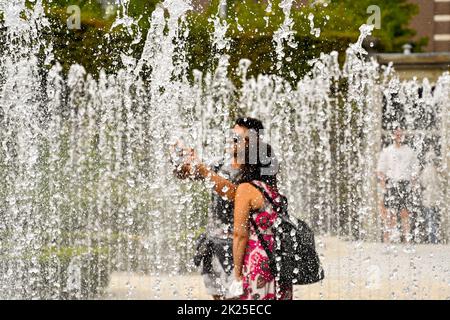 Amsterdam, Paesi Bassi - Agosto 2022: Due persone prendono un selfie mentre si trovano in mezzo a una fontana in un giardino pubblico Foto Stock