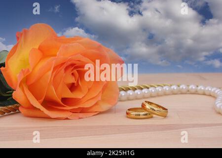 Rosa arancione con anelli e perle d'oro per matrimoni Foto Stock