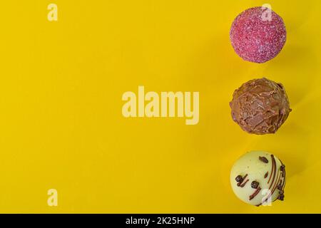 Collezione di dolci al cioccolato su sfondo colorato. Praline al cioccolato su sfondo giallo con spazio copia. Piano di giacitura, vista dall'alto Foto Stock