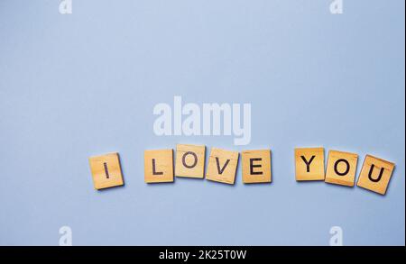 Iscrizione ti amo in lettere di legno su sfondo blu. Cartolina pronta, banner, posto per un'iscrizione. Foto Stock