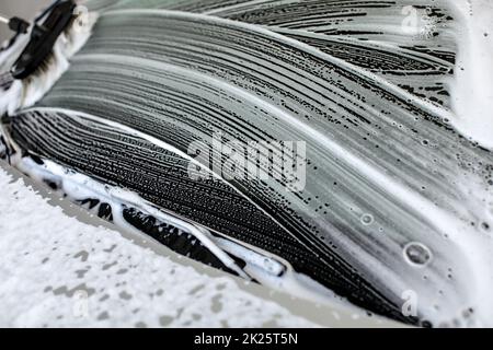 Pennello lasciando tratti in shampoo e schiuma sul parabrezza della vettura lavata al self service autolavaggi. Foto Stock