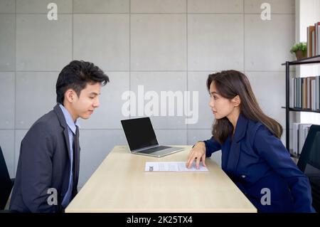 Il giovane manager asiatico in Blue Suit chiede il profilo di un candidato durante un'intervista. L'atmosfera del colloquio di lavoro nel moderno ufficio. Foto Stock