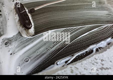 Pennello lasciando tratti in schiuma bianca sul parabrezza di un auto lavata in carwash Foto Stock