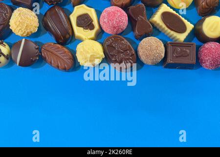 Praline al cioccolato frame vista dall'alto immagini stock. Caramelle al cioccolato su sfondo blu. Vista dall'alto della cornice Chocolate. Praline di cioccolato sfondo con spazio di copia per il testo. Confine di diverse caramelle Foto Stock