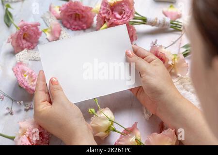 Le mani della donna che tengono la scheda vuota sopra i fiori su un tavolo Foto Stock
