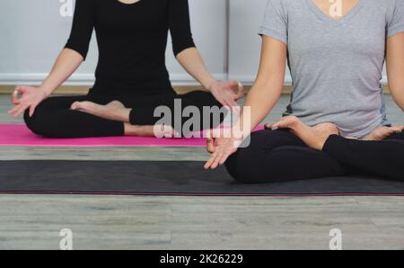 Le donne che fanno l'esercitazione meditating di yoga nella posizione del loto con il mudra durante la lezione di yoga. Allenati indossando una camicia nera e pantaloni bianchi. Concetto di assistenza sanitaria.. Foto Stock