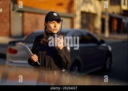 Donna della polizia che parla usando walkie-talkie durante il pattugliamento Foto Stock