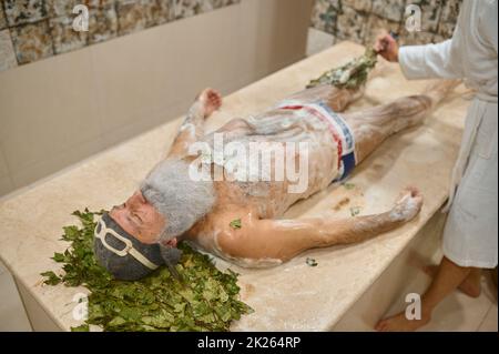 Uomo anziano che ottiene massaggio con scopa di quercia Foto Stock