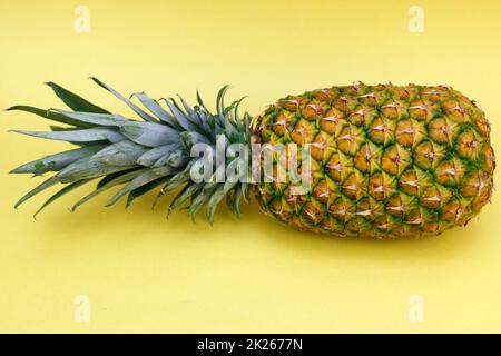 Ananas intero con Top che si posa lateralmente su sfondo giallo Foto Stock