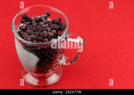 Frutti di bosco congelati in una tazza di vetro primo piano su sfondo rosso Foto Stock