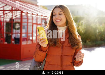 Giovane donna che usa il telefono a piedi in città nella soleggiata giornata invernale Foto Stock