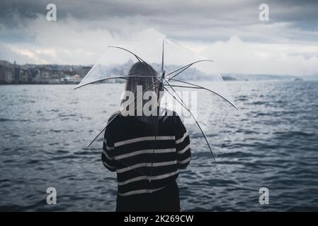 donna che tiene un ombrello trasparente davanti all'acqua Foto Stock