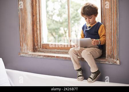 HES tech savvy già. Un ragazzino carino che usa un tablet mentre si siede su un davanzale. Foto Stock