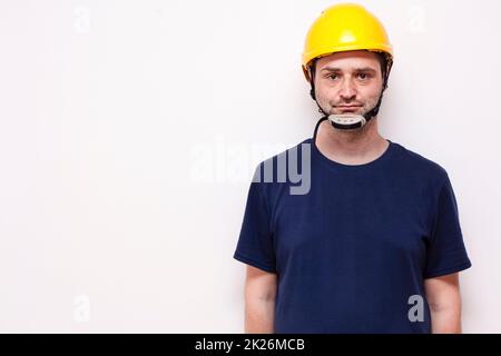 Lavoratore di costruzione dietro sfondo bianco. Indossare maschera verde e casco giallo Foto Stock