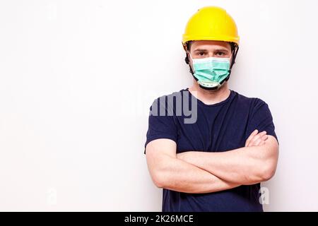 Lavoratore di costruzione dietro sfondo bianco. Indossare maschera verde e casco giallo Foto Stock