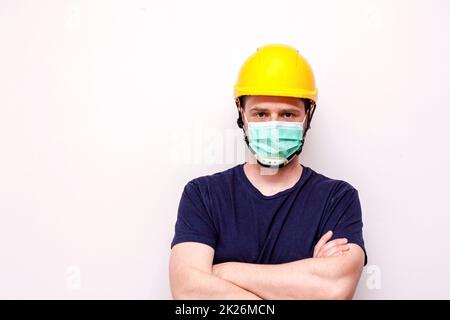 Lavoratore di costruzione dietro sfondo bianco. Indossare maschera verde e casco giallo Foto Stock