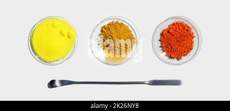 Ossido di piombo (II,IV), cromatura di potassio e curcuma organico in polvere in vetro chimico posto accanto alla spatola in acciaio inossidabile. Ingrediente chimico di primo piano su tabella bianca del laboratorio. Vista dall'alto Foto Stock