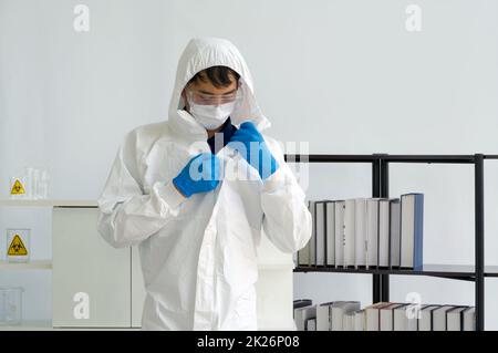 Scienziato asiatico con maschera viso indossare indumenti protettivi virus prima di iniziare l'esperimento in un laboratorio scientifico. Foto Stock