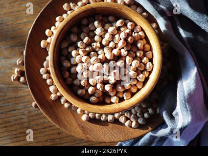 Ceci secchi non cotti in ciotola di legno su tavola rustica di legno. Mucchio di legume ceci sfondo Foto Stock