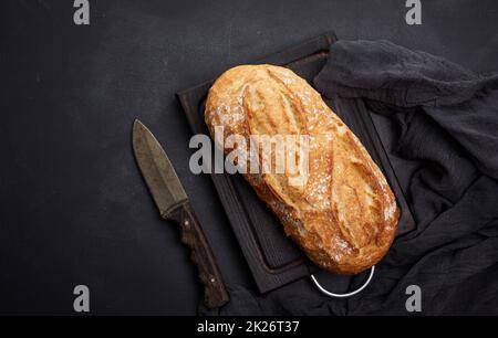 pane ovale intero cotto a forno a base di farina di grano bianco su un tavolo nero, vista dall'alto Foto Stock