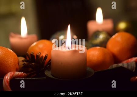 Tre candele brucianti con mandarini e un cono di pino come decorazione di natale Foto Stock