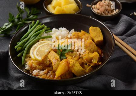 Un curry di Massaman di pollo in ciotola nera su fondo scuro. Il Massaman Curry è il miglior piatto tailandese indiano con carne di pollo, patate, cipolla e molte spezie è influenzato dalle culture musulmane malesi e thailandesi. Foto Stock