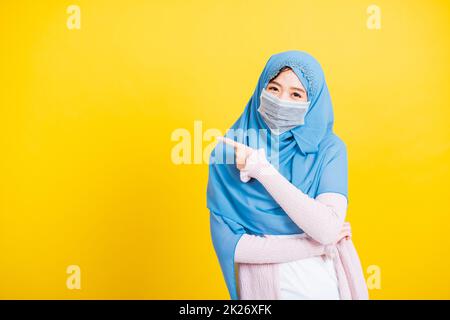 Donna indossare hijab e maschera di protezione del viso per prevenire coronavirus che punta dito lato lontano Foto Stock