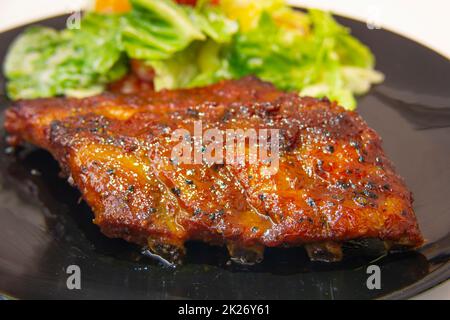 Primo piano di deliziose costolette di maiale al barbecue con verdure sul piatto basso DOF Foto Stock