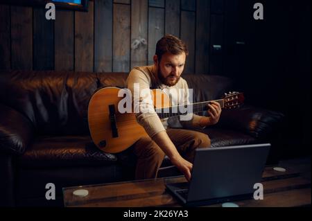 Giovane uomo che impara a suonare la chitarra attraverso internet Foto Stock