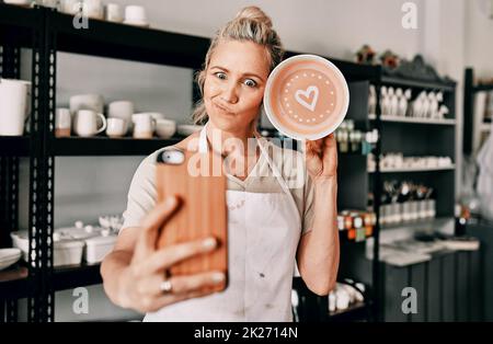 Ecco il look finale. Scatto corto di una donna matura attraente usando il suo cellulare per prendere un selfie con la sua ceramica nel suo studio. Foto Stock